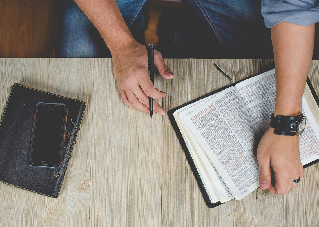 Person holding Bible with phone and journal on table