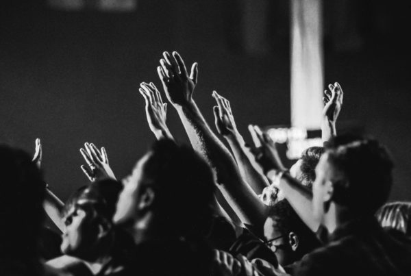 black and white photo of hands raised in church with people singing