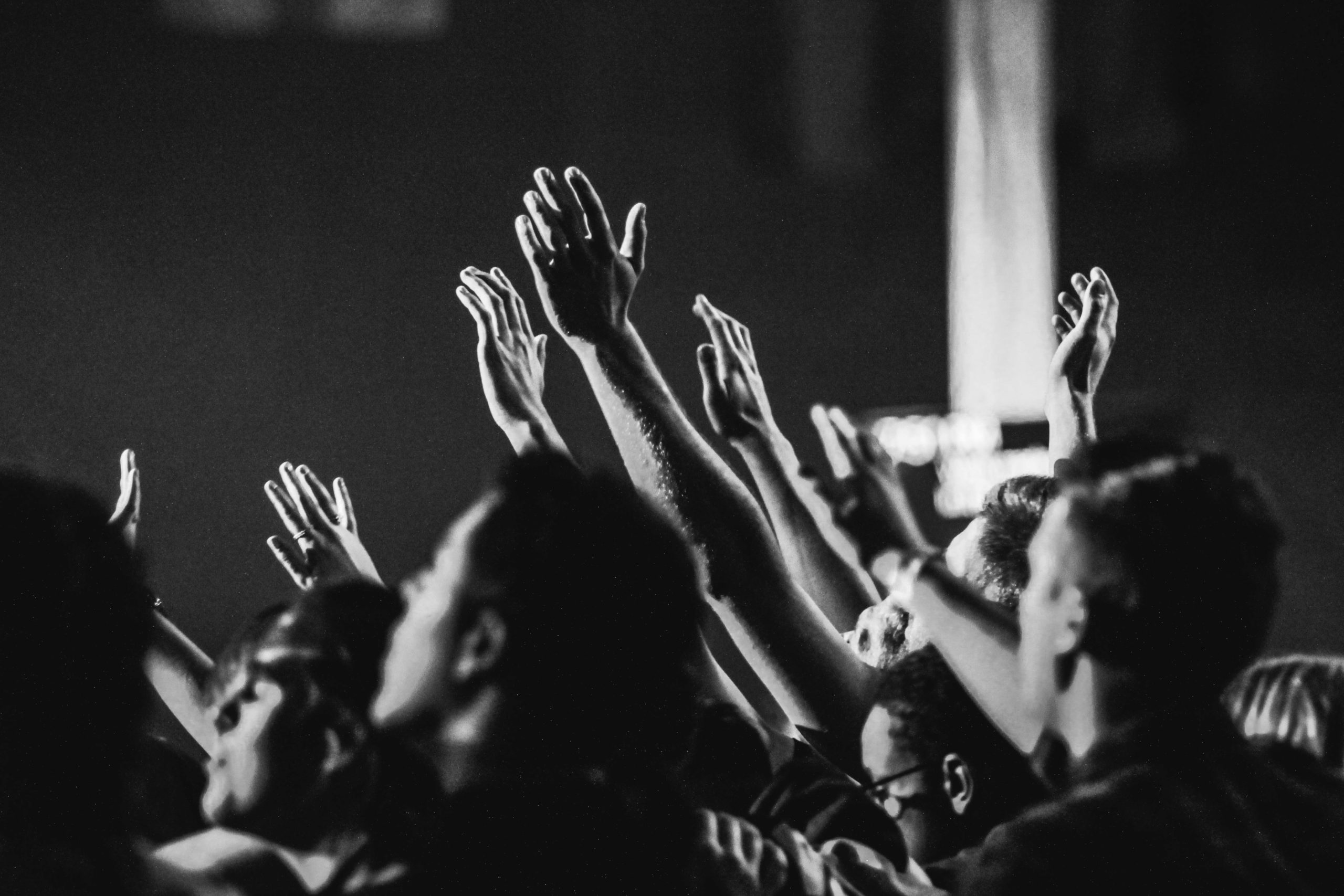 black and white photo of hands raised in church with people singing